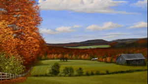 A rich autumn landscape featuring a foreground of green grass with a dark barn on the right and a white wooden fence on the left, looking out over a valley where the trees are ablaze with orange and red fall foliage against dark hills under a blue, cloudy sky.